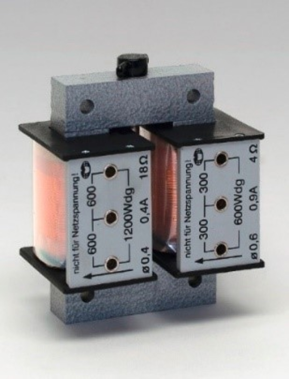 Das Bild zeigt eine elektrische Spule mit zwei Wicklungen, die auf einer stabilen Basis montiert ist. Die Spule verf&uuml;gt &uuml;ber mehrere Anschl&uuml;sse, die f&uuml;r Experimente im Bereich der Elektrotechnik und Physik genutzt werden k&ouml;nnen.