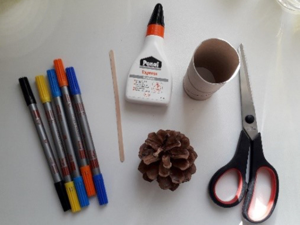 Das Bild zeigt eine Sammlung von Bastelmaterialien, darunter bunte Filzstifte, eine Flasche Kleber, eine Schere, einen Bastelholzstab und eine Kiefernnuss. Außerdem ist ein Papprollkörper abgebildet, der für kreative Projekte genutzt werden kann.