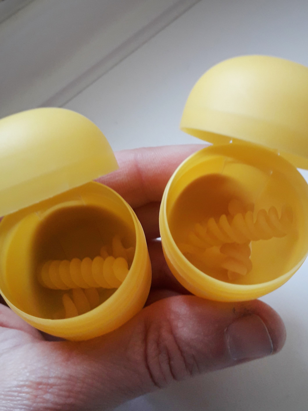 Zwei gelbe, halbkugelige Behälter sind geöffnet und zeigen eine spiralförmige Innengestaltung (jeweils eine Nudel liegt innen).