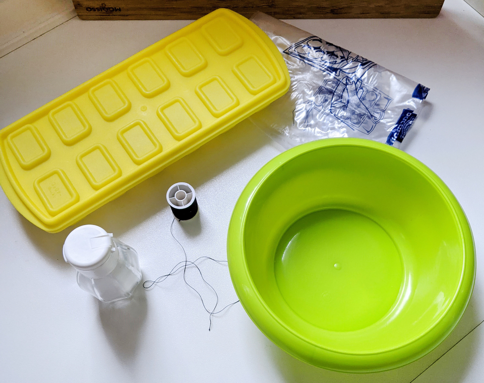 Das Bild zeigt eine Sammlung von Experimentiermaterialien, darunter eine gr&uuml;ne Sch&uuml;ssel, eine gelbe Silikonform, eine kleine Glasflasche und einen Garnrollen. Diese Gegenst&auml;nde sind f&uuml;r verschiedene Bildungs- und Experimentieraktivit&auml;ten gedacht.