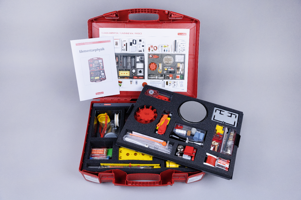 Das Bild zeigt einen roten Koffer voller Experimentiermaterialien für den Bereich Elementarphysik, einschließlich verschiedener Werkzeuge und Komponenten. Zudem liegt ein Lehrbuch mit Informationen zu den Inhalten und Experimenten auf dem Koffer.