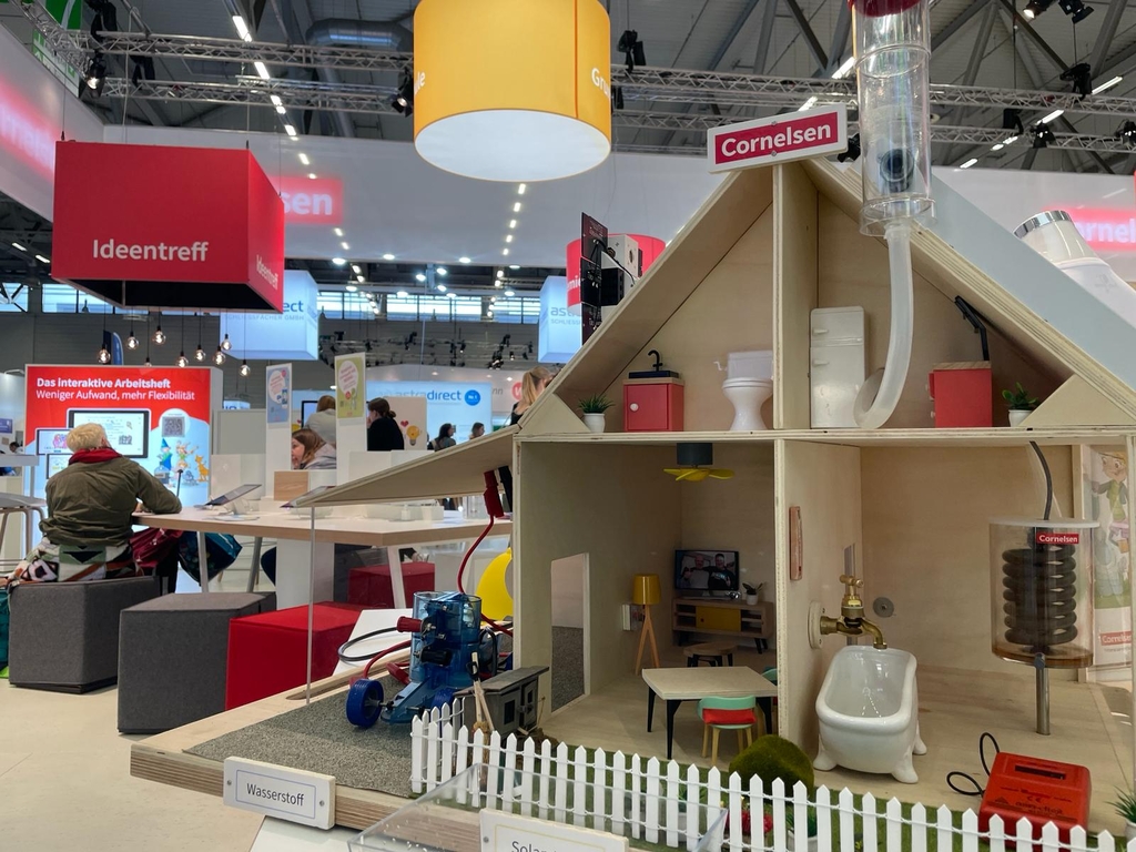 Das Bild zeigt ein Modell eines Energiewandelhauses, das mit verschiedenen Modulen rund um das Thema Solarenergie ausgestattet ist. Das Haus verf&uuml;gt &uuml;ber eine M&ouml;blierung sowie &uuml;ber Installationen, einschlie&szlig;lich eines Wasserstoffgenerators im Au&szlig;enbereich