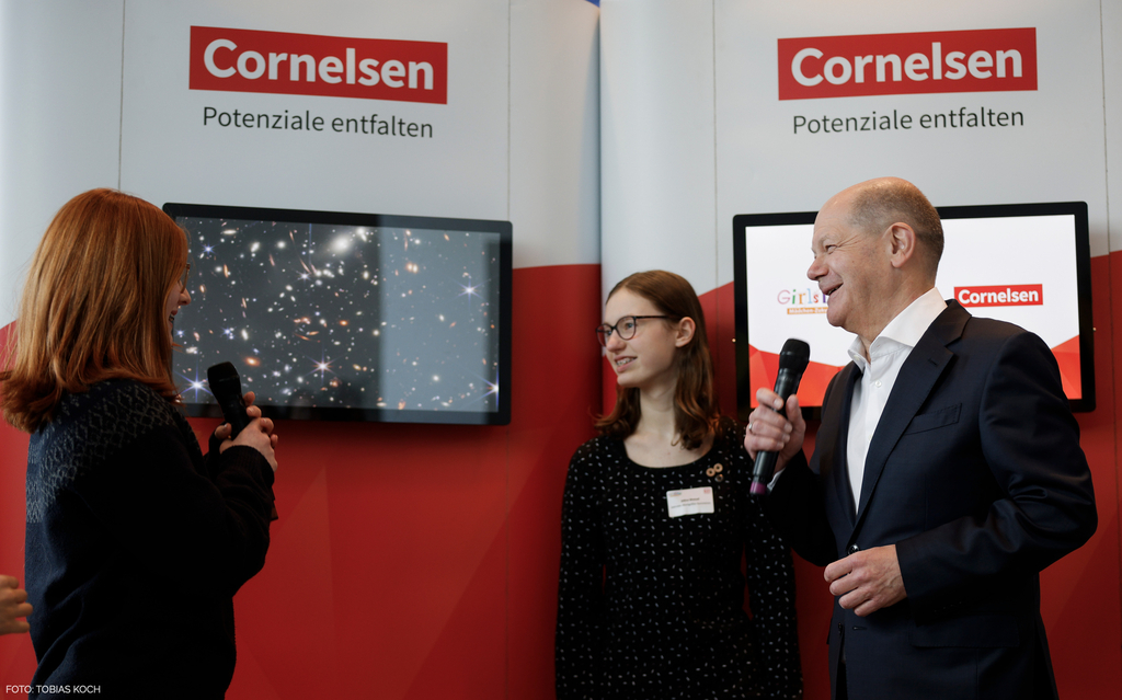 Olaf Scholz steht l&auml;chelnd mit einem Mikrofon in der Hand neben zwei Sch&uuml;lerinnen bei der Auftaktveranstaltung zum Girls' Day 2024 im Bundeskanzleramt.