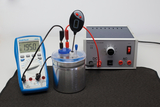 Das Bild zeigt ein Experimentieraufbau mit einem Multimeter, einem Stromversorgungseinheit und einem Behälter, der wahrscheinlich für chemische Experimente genutzt wird. Der Multimeter misst eine Stromstärke von 1,950 A, während die Stromversorgung sowohl