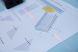 Das Bild zeigt einen durchsichtigen Block, der auf einem Arbeitsblatt mit geometrischen Zeichnungen platziert ist. Ein Laserstrahl verläuft durch den Block und trifft auf das Arbeitsblatt, um optische Phänomene wie Lichtbrechung zu demonstrieren.