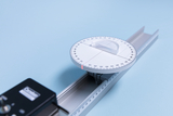 Das Bild zeigt ein Experimentiergerät, das aus einem Protractor (Winkelmesser) und einer Schiene besteht. Der Winkelmesser ist präzise skaliert und ermöglicht das Messen und Anlegen von Winkeln für verschiedene mathematische und physikalische Anwendungen.