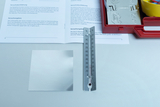 Das Bild zeigt ein Thermometer, ein silbernes Metallblatt und ein offenes Handbuch auf einem Tisch. Die Materialien sind Teil eines Experiments, das sich mit der Wärmeleitung und Reflexion von Lichtstrahlen beschäftigt.