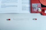 Das Bild zeigt ein Experimentier-Set mit einem Reagenzglas, zwei Magneten und einer roten Box, die weitere Materialien enthält. Ein Handbuch mit den Versuchsanleitungen liegt daneben und beschreibt die magnetischen Effekte, die im Experiment beobachtet we