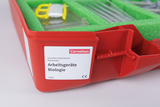 Das Bild zeigt einen roten Kasten mit dem Etikett „Arbeitsgeräte Biologie“ von Cornelsen, der für den Einsatz im Bildungswesen konzipiert ist. Im Inneren befinden sich verschiedene experimentelle Materialien, eingebettet in grünes Schaumstoffmaterial.