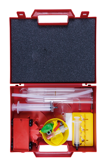Das Bild zeigt einen roten Kasten voller Experimentiermaterialien, darunter Spritzen, Röhren und verschiedene kleine Objekte wie einen Wagen und bunte Ballons. Diese Materialien sind für wissenschaftliche Experimente im Bildungsbereich konzipiert.