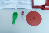 Das Bild zeigt eine grüne Latexblase, ein Ventil und eine rote Plattform, die Teil eines Experimentierkits ist. Dieses Set wird zur Demonstration von Luftdruck und Bewegung in Bildungssettings verwendet.