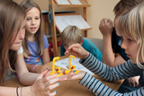 Das Bild zeigt eine Gruppe von Kindern, die an einem Tisch sitzen und gemeinsam an einem Experiment arbeiten. Sie halten gelbe Modelle in den Händen, während sie sich konzentriert miteinander austauschen und das Experimentieren genießen.