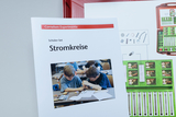 Das Bild zeigt ein Schüler-Set zum Thema Stromkreise aus dem Cornelsen Experimenta Sortiment. Auf dem Titelblatt des Heftes sind zwei Kinder beim Experimentieren abgebildet, während daneben eine Übersicht über das darin enthaltene Material zu sehen ist.