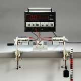 Das Bild zeigt ein Laborgerät mit einem digitalen Multimeter, das zur Messung elektrischer Werte eingesetzt wird. An beiden Seiten sind Motoren montiert, die mit einer Gewichtsaufhängung verbunden sind, um Experimente zur Elektromechanik durchzuführen.