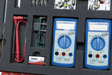 Das Bild zeigt ein Set von zwei blauen Multimetern in einem Schaumstoffeinleger. Neben den Multimetern sind verschiedene Kabel, Messspitzen und eine 9V-Batterie angeordnet, die für experimentelle Anwendungen im Bildungswesen verwendet werden können.