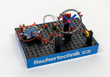 Das Bild zeigt ein Experimentiermodell von fischertechnik, das mit einer Motorsteuerung und farbigen Kabeln ausgestattet ist. Es beinhaltet einen Propeller und eine Basisplatte, die für praktische elektrische und mechanische Experimente im Bildungsbereich
