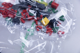 Auf dem Bild sind verschiedene elektronische Bauteile in einer transparenten Plastiktüte zu sehen. Die Teile umfassen rote, grüne, schwarze und gelbe Steckverbinder sowie Schrauben, die für Experimente im Bildungsbereich verwendet werden können.