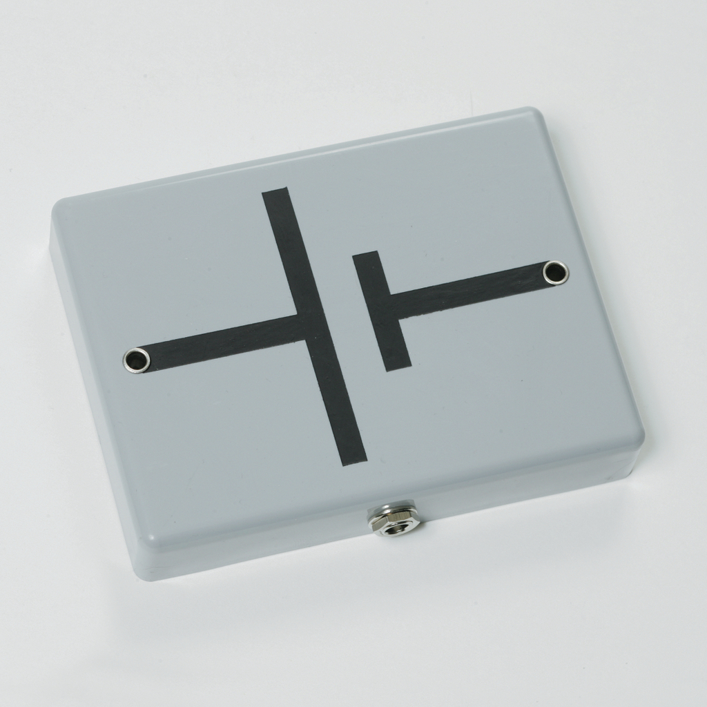 Das Bild zeigt ein graues Gehäuse mit einer schwarzen Schaltung, die anscheinend eine elektrische Schaltung darstellt. An der Unterseite befinden sich zwei Anschlüsse, die für Experimentierzwecke in der Elektrotechnik verwendet werden können.