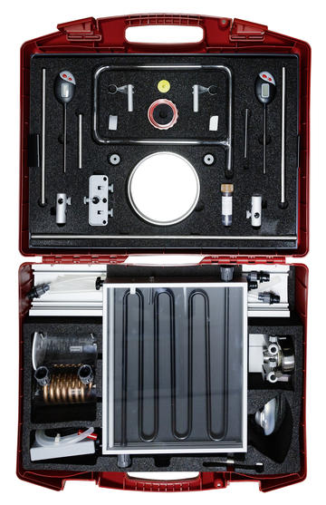 Das Bild zeigt einen offenen roten Koffer, der verschiedene wissenschaftliche Experimentierwerkzeuge und -geräte enthält. Dazu gehören Rohre, Messgeräte, Ventile und ein Solarabsorber, die für Bildungszwecke im naturwissenschaftlichen Unterricht verwendet