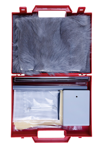 Das Bild zeigt einen roten Koffer, der verschiedene Experimentiermaterialien enthält. Dazu gehören ein graues Fellstück, Röhren, ein Netz, eine kleine Box und weitere Utensilien, die für Bildungszwecke im Experimentierbereich verwendet werden können.