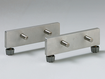 Das Bild zeigt zwei metallische Teile, die parallel zueinander angeordnet sind. Jedes Teil hat mehrere Stifte und ist auf einem stabilen Untergrund mit verstellbaren Füßen montiert, wahrscheinlich für physikalische Experimente.