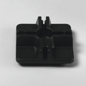 Das Bild zeigt ein quadratisches, schwarzes Kunststoffteil mit abgerundeten Ecken und vertieften Bereichen. Es scheint sich um eine Halterung oder Basis zu handeln, die möglicherweise für experimentelle Setups im Bildungsbereich verwendet wird.