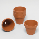 Das Bild zeigt mehrere terrakottafarbene Blumentöpfe, die unterschiedlich aufgestellt sind. Ein Topf liegt auf dem Kopf, während die anderen aufrecht auf einem weißen Hintergrund gestapelt sind.