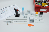Das Bild zeigt eine Sammlung von Experimentiermaterialien, darunter einen Handbrenner, eine digitale Waage, chemische Substanzen und verschiedene Laborwerkzeuge. Im Hintergrund liegen Anleitungshefte, die die Nutzung der Geräte und Materialien beschreiben.