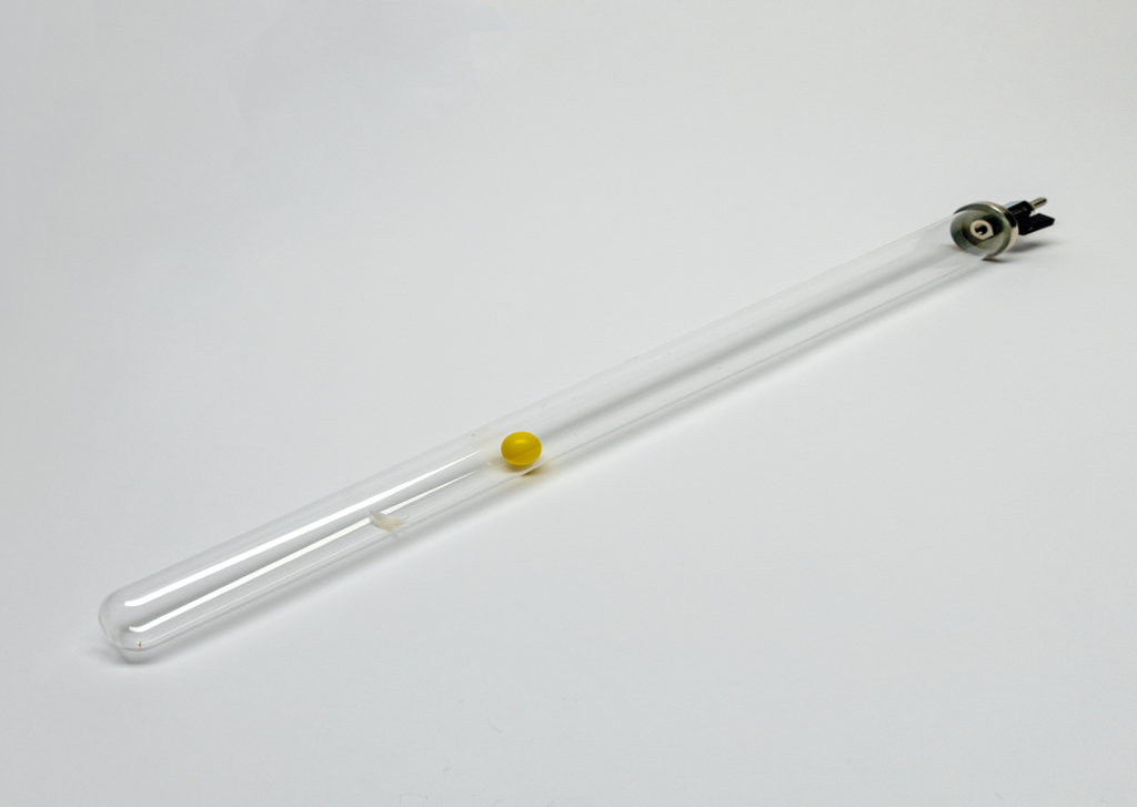 Das Bild zeigt ein transparentes Glasröhrchen mit einer gelben Kugel im Inneren. Das Röhrchen hat an einem Ende einen Anschluss, wahrscheinlich für Experimentierzwecke im Bildungsbereich.