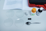 Das Bild zeigt verschiedene Laborausrüstungen, darunter zwei Petrischalen, Chemikalien wie Zucker und Jodlösung sowie ein Tropfer und einen Löffel. Im Hintergrund ist ein Informationsheft zu sehen, das vermutlich Anleitungen für Experimentieraufbauten enthält.
