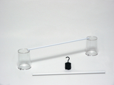 Das Bild zeigt zwei transparente Becher, die durch einen weißen Schlauch verbunden sind, sowie ein schwarzes Gewicht und einen weiteren weißen Schlauch. Diese Materialien könnten für chemische Experimente oder physikalische Versuche im Bildungsbereich verwendet werden.