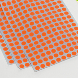 Das Bild zeigt mehrere Blätter mit einer Vielzahl von orangefarbigen Punkten, die gleichmäßig auf einer transparenten Unterlage verteilt sind. Diese Punkte könnten als Aufkleber oder zur Beschriftung verwendet werden, wodurch sie für experimentelle Zwecke im Bildungswesen nützlich sind.