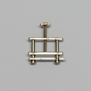 Das Bild zeigt einen kleinen Metallverspanner, der aus mehreren horizontalen und vertikalen Stangen sowie einer drehbaren Schraube besteht. Er wird häufig in experimentellen Anwendungen verwendet, um Objekte fixiert zu halten.