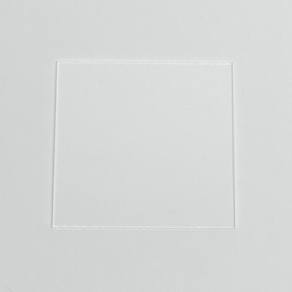 Das Bild zeigt eine klare, rechteckige Folie, die in einen weißen Hintergrund eingelassen ist. Diese Folie könnte Teil eines Setups für Experimente im Bildungsbereich sein, um verschiedene Materialien oder Reaktionen zu beobachten.