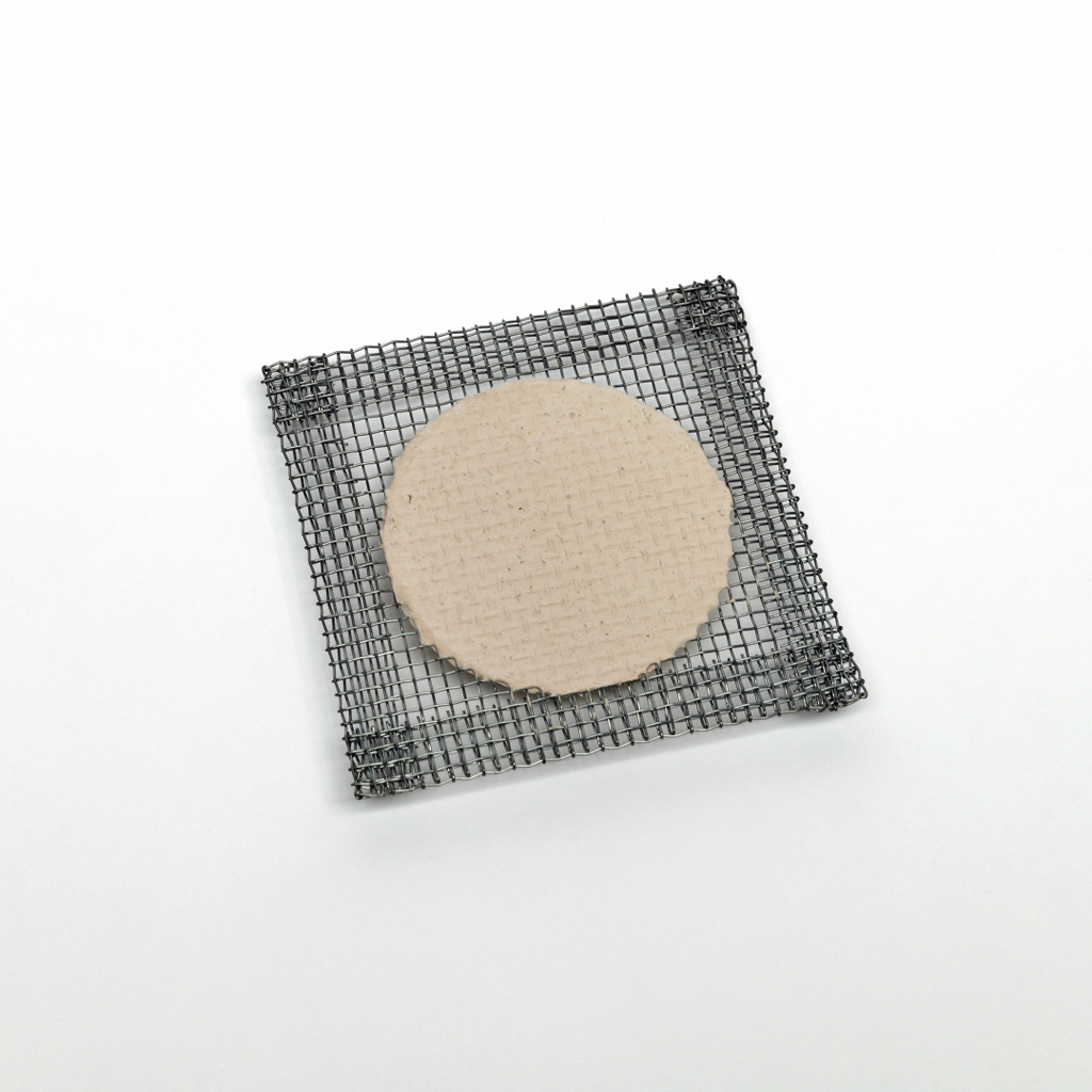 Das Bild zeigt eine quadratische Drahtgitterplatte, die eine runde Pappe in der Mitte hält. Diese Materialien könnten für verschiedene Experimente im Bildungsbereich verwendet werden, etwa in der Chemie oder Physik.