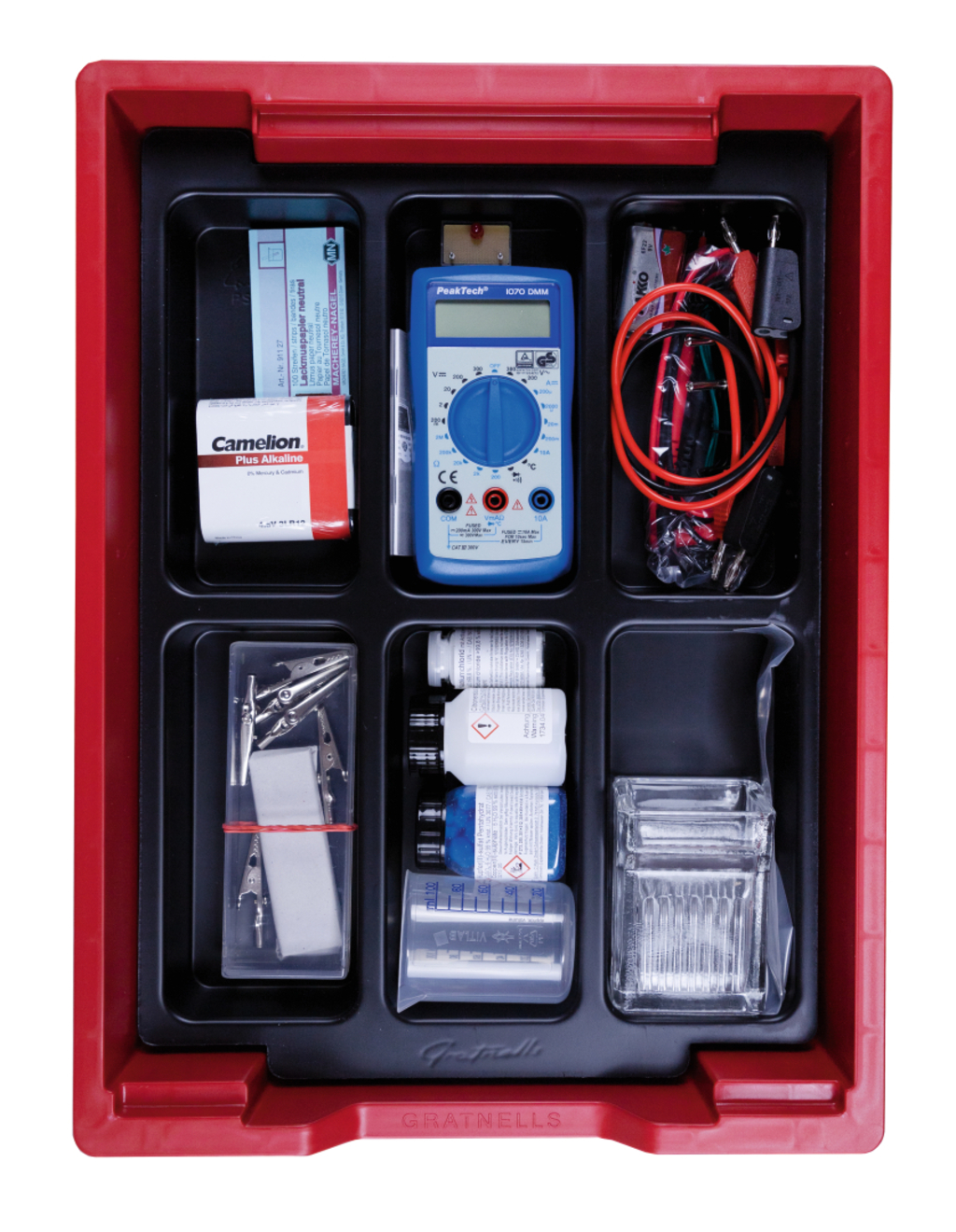 Das Bild zeigt eine rote Aufbewahrungsbox, die verschiedene Experimentiermaterialien enthält, darunter ein Multimeter, Alkaline-Batterien, Kabel, Zangen sowie Chemikalien in Flaschen. Die Anordnung der Utensilien ist übersichtlich, um den Einsatz im Bildungsbereich zu erleichtern.