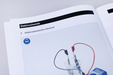 Das Bild zeigt eine Seite aus einem Lehrbuch zum Thema Elektrochemie, die ein elektrochemisches Element beschreibt. Zu sehen sind ein transparentes Behältnis mit Elektroden und Kabeln sowie ein Messgerät zur Anzeige von Werten.