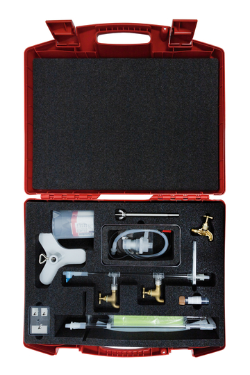 Das Bild zeigt einen roten Transportkoffer, der mit verschiedenen Experimentiergeräten für den Unterricht gefüllt ist. Die Ausstattung umfasst unter anderem Röhrchen, Ventile und eine Spritze, die für praktische wissenschaftliche Experimente verwendet werden können.