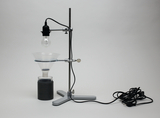 Das Bild zeigt ein Experimentiergerät mit einer Lampenfassung, die über einem Trichter montiert ist. Darunter befindet sich ein schwarzer Behälter, der wahrscheinlich für chemische Experimente oder als Teil eines physikalischen Versuchs verwendet wird.