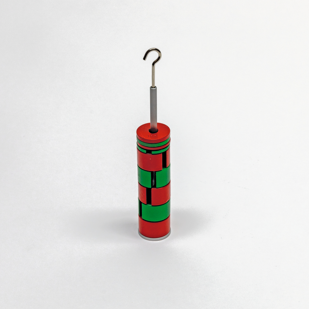 Das Bild zeigt ein zylindrisches Experimentiergerät, das in rot und grün lackiert ist und einen metallischen Haken an der Spitze aufweist. Es scheint für physikalische Experimente im Bildungsbereich konzipiert zu sein.