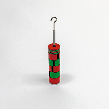 Das Bild zeigt ein zylindrisches Experimentiergerät, das in rot und grün lackiert ist und einen metallischen Haken an der Spitze aufweist. Es scheint für physikalische Experimente im Bildungsbereich konzipiert zu sein.