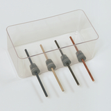 Das Bild zeigt eine transparente Box mit vier unterschiedlichen Stäben, die in grauen Haltern fixiert sind. Die Stäbe bestehen aus verschiedenen Materialien und Farben, möglicherweise für experimentelle Zwecke im Bildungsbereich.