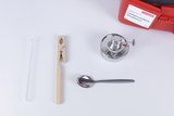 Das Bild zeigt eine Anordnung von Experimentiermaterialien, darunter ein Reagenzglas, eine Holzklammer, ein Spirituskocher und ein Esslöffel aus Edelstahl. Diese Utensilien sind typischerweise für naturwissenschaftliche Experimente im Bildungsbereich vorgesehen.