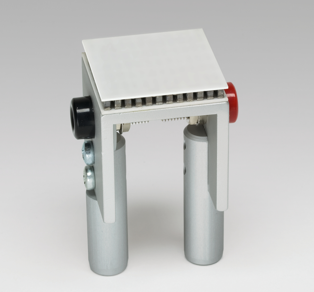 Das Bild zeigt ein Experimentiergerät mit einer quadratischen Plattform und zwei zylindrischen Stützen. Es dient vermutlich der Durchführung von physikalischen Experimenten im Bildungsbereich und ist aus Metall gefertigt.