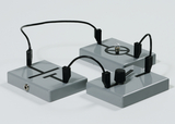 Das Bild zeigt drei graue Platten mit verschiedenen Symbolen und elektrischen Verbindungen. Eine der Platten enthält eine kleine Glühbirne, während eine andere über einen Drehregler verfügt, was auf eine experimentelle Verwendung im Bildungsbereich hinweist.