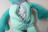 Das Bild zeigt ein teal-farbenes Stofftier mit einem Reißverschluss entlang der Seite. Der Reißverschluss ist geöffnet, und im Inneren ist ein Etikett sichtbar, das Informationen zur Herstellung enthält.