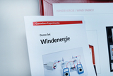 Das Bild zeigt eine Anleitung für ein Demo-Set zum Thema Windenergie, herausgegeben von Cornelsen Experimenta. Im Hintergrund sind Geräte und Kabel abgebildet, die zur Durchführung von Experimenten zur Windenergienutzung dienen.