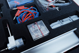 Das Bild zeigt ein Experimentierkasten mit verschiedenen Komponenten, darunter Kabel in blau und rot, einen kleinen Motor und einige transparente Bauteile. Alles ist ordentlich in einem schwarz gepolsterten Fach angeordnet, das eine sichere Aufbewahrung gewährleistet.