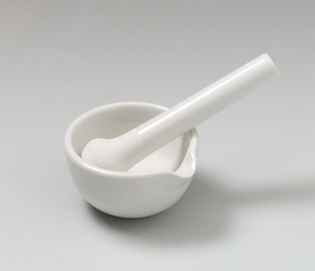 Das Bild zeigt einen weißen Mörser und einen Stößel, die aus Keramik gefertigt sind. Diese Geräte werden in chemischen Experimenten verwendet, um Stoffe zu zerkleinern oder zu vermischen.