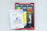 Das Bild zeigt ein Experimentier-Kit für Kinder, das Materialien zur Durchführung von Experimenten mit Elektrizität enthält. Neben dem Inhalt ist ein Heft zu sehen, das Anleitungen für die Experimente bietet und sich an Kindergartenkinder richtet.